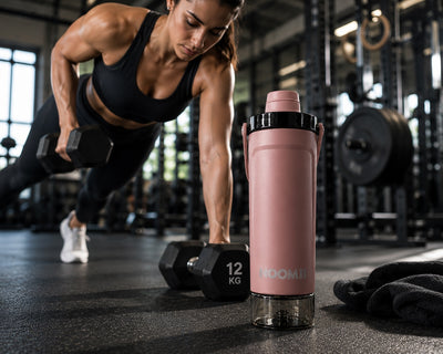 Frau beim Hanteltraining im Gym mit dem NooMii ProShake 600 in Bronze im Vordergrund